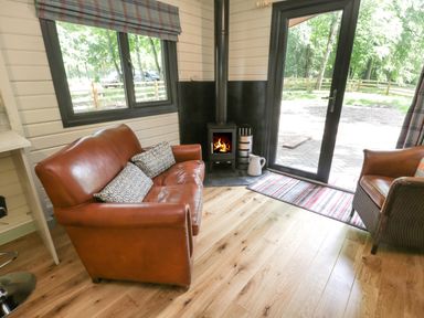 A room with a brown leather sofa and armchair wooden floor a stove and glass door at Lake View Lodge in Wykeham near East Ayton