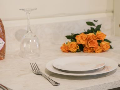 A kitchen counter with two stacked plates a fork an upside down wine glass a bottle and orange roses at Lake View Lodge in Wykeham near East Ayton