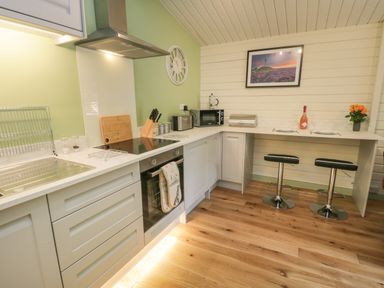 A kitchen with a sink stovetop oven microwave and two stools at Lake View Lodge Wykeham near East Ayton