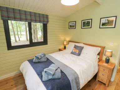 A bedroom with a bed with white bedding and blue towels on it two bedside tables with lamps and three framed pictures on the wall at Lake View Lodge in Wykeham near East Ayton