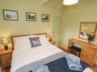 A bedroom with a double bed bedside tables lamps a wooden dressing table with mirror and flowers at Lake View Lodge in Wykeham near East Ayton