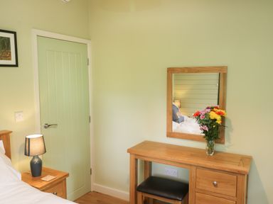 A bedroom corner with a wooden desk mirror flowers and a bedside lamp at Lake View Lodge in Wykeham near East Ayton