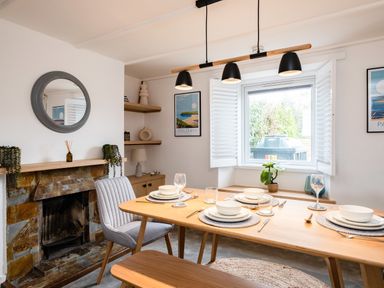 A dining room with a wooden table set for four near a window and a stone fireplace at West Cottage in Rock
