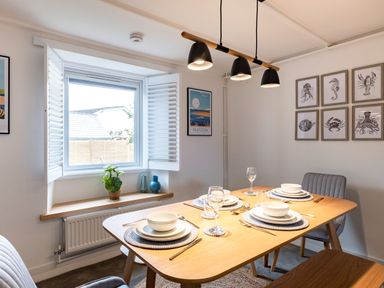 A dining room with a wooden table set for four under pendant lights by a window with shutters at West Cottage in Rock