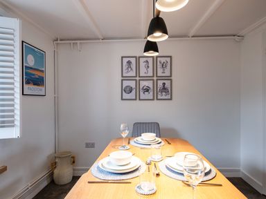A dining room with a wooden table set for three and framed sea creature prints on the wall at West Cottage in Rock