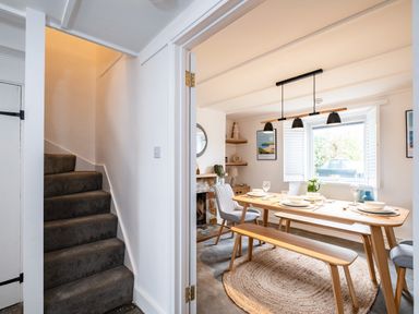 A dining room with a wooden table set for four people and a staircase with carpet next to it at West Cottage in Rock