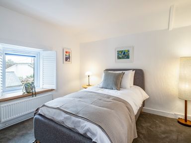A bedroom with a single bed bedside table with a lamp window with shutters and a plant at West Cottage in Rock
