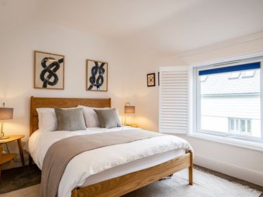 A bedroom with a wooden bed frame two bedside tables with lamps and three framed artworks above the bed at West Cottage in Rock