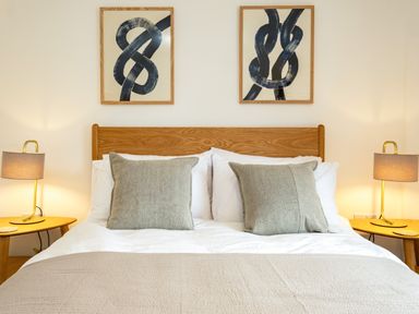 A bedroom with a wooden bed frame two large pillows and two bedside tables with lamps at West Cottage in Rock