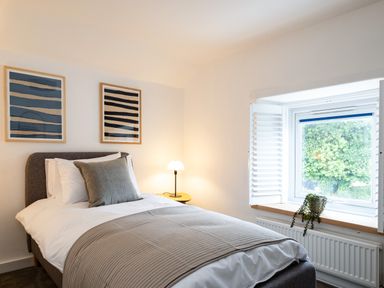 A bedroom with a single bed a bedside table with a lamp two framed artworks and a window with shutters at West Cottage in Rock