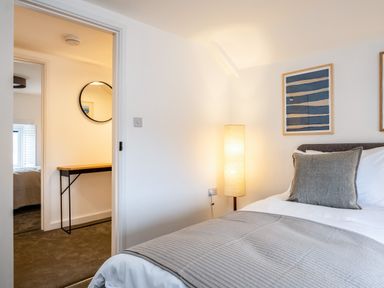 A bedroom with a bed blanket and pillow a floor lamp and framed artwork at West Cottage in Rock