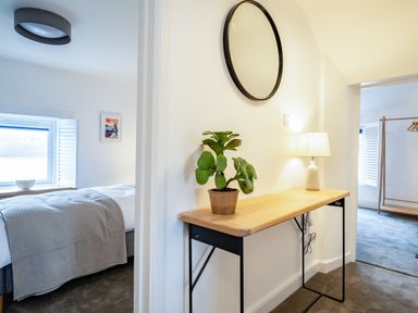 A hallway with a wooden console table holding a potted plant and table lamp with a round mirror above and bedrooms visible at West Cottage in Rock