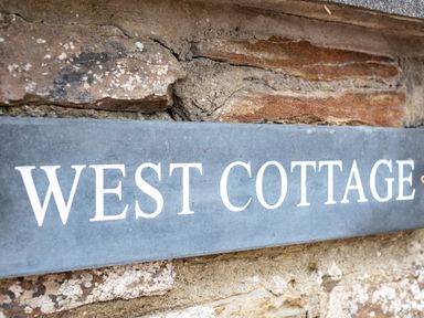 A close up of a blue sign with white text saying West Cottage mounted on a stone wall at West Cottage Rock