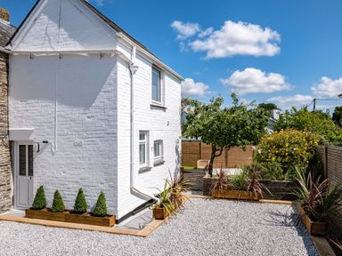 An outdoor area with a white brick house on the left and a garden with plants and trees surrounded by wooden fences at West Cottage in Rock