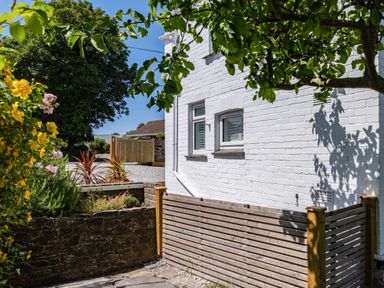 Exterior side of a white brick house with wooden fencing plants and trees at West Cottage in Rock