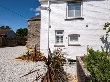 Exterior of a white brick house with three windows gravel ground and planted garden boxes at West Cottage in Rock