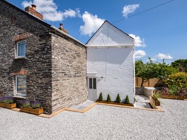Exterior of a stone and white brick house with gravel ground and small landscaped plants at West Cottage in Rock