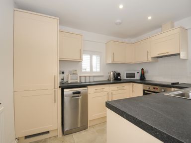 A kitchen with cream cabinets black countertops stainless steel dishwasher microwave oven and a small window at West Cottage in Rock