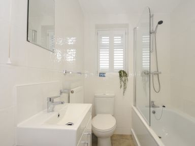 A bathroom with a sink a toilet a bathtub with a shower and a window with shutters at West Cottage in Rock