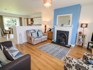 A living room with sofas a fireplace and a dining area with chairs in the background at 4 The Cloisters in Bushmills County Antrim