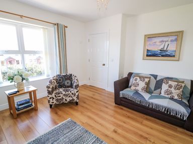 A living room with a sofa a patterned armchair a small wooden table and a painting of a sailboat at 4 The Cloisters in Bushmills County Antrim