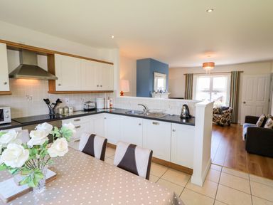 A kitchen with white cabinets and a dining table with a vase of white flowers at 4 The Cloisters in Bushmills County Antrim