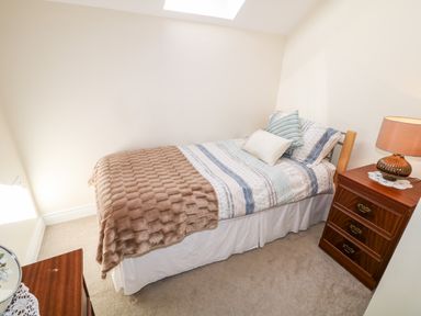 A bedroom with a single bed with pillows and blanket a wooden chest of drawers with a lamp at 4 The Cloisters in Bushmills County Antrim