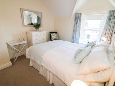 A bedroom with a bed, chest of drawers, mirror, window with curtains, and a small side table with a teddy bear at 4 The Cloisters in Bushmills County Antrim
