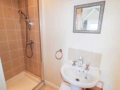 A bathroom with a tiled shower and a white sink with a mirror above at 4 The Cloisters in Bushmills County Antrim