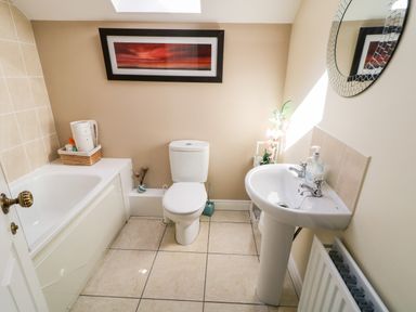 A bathroom with a bathtub a toilet a pedestal sink a round mirror and a framed picture above the toilet at 4 The Cloisters in Bushmills County Antrim