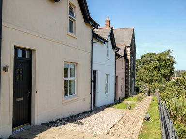 A row of connected houses with front doors and windows along a paved walkway at 4 The Cloisters in Bushmills County Antrim