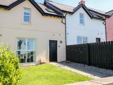 A row of terraced houses with front doors and windows and a small green lawn at 4 The Cloisters in Bushmills County Antrim
