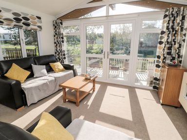 A living room with two black sofas and a wooden coffee table near large glass doors at Pinecone Lodge - No 9 Felmoor Park near Felton