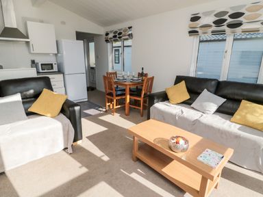 A living room with black sofas yellow and grey cushions a wooden coffee table and a dining table with four chairs at Pinecone Lodge - No 9 Felmoor Park near Felton