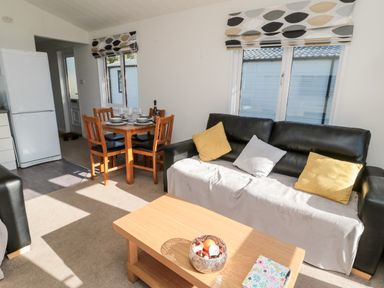 A living room with a black sofa and yellow and gray cushions near a wooden coffee table and dining table at Pinecone Lodge - No 9 Felmoor Park near Felton