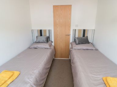 A bedroom with two single beds with striped headboards and yellow towels at Pinecone Lodge - No 9 Felmoor Park near Felton