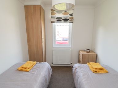 A bedroom with two single beds with yellow towels a wardrobe a chest of drawers and a window at Pinecone Lodge - No 9 Felmoor Park near Felton