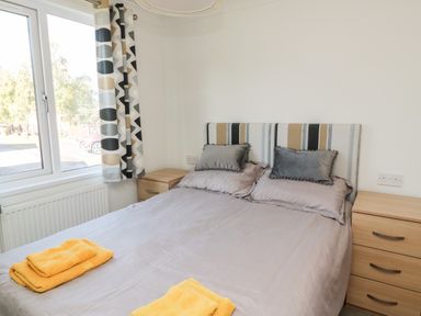 A bedroom with a double bed wooden bedside tables and a window with patterned curtains at Pinecone Lodge - No 9 Felmoor Park near Felton