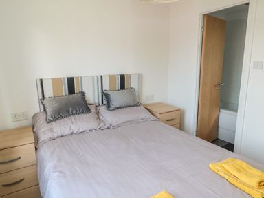 A bedroom with a bed with pillows and folded towels and bedside cabinets with drawers at Pinecone Lodge - No 9 Felmoor Park near Felton
