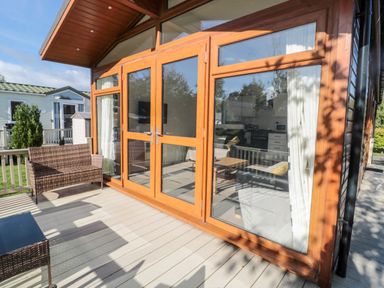 An outdoor deck with wicker furniture and large glass doors leading to a living area at Pinecone Lodge - No 9 Felmoor Park near Felton