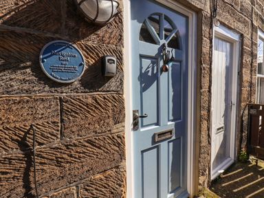 A blue front door with a sea creature door knocker and a blue plaque on a stone wall at Navigators Rest in Whitby