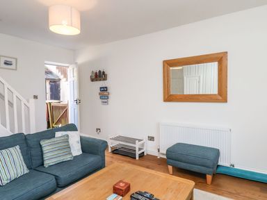 A living room with a blue sofa and ottoman a wooden coffee table a wall mirror and an open door at Navigators Rest in Whitby