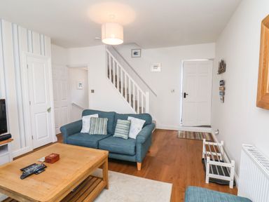A living room with a blue couch coffee table remote controls and stairs in the background at Navigators Rest in Whitby