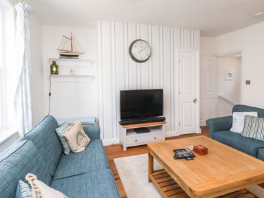 A living room with blue sofas a wooden coffee table a television on a stand and striped wallpaper at Navigators Rest in Whitby