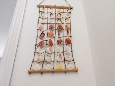 A wall hanging made of shells attached to a rope grid on a white wall at Navigators Rest in Whitby
