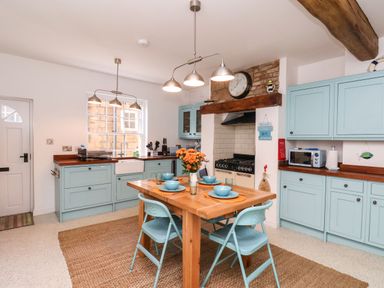 A kitchen with blue cabinets wooden countertops a wooden dining table with blue chairs and tableware at Navigators Rest in Whitby