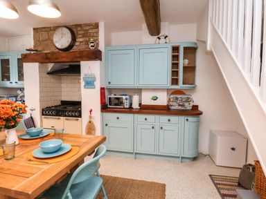 A kitchen with light blue cabinets a wooden dining table set with blue bowls and a clock above a stove at Navigators Rest in Whitby