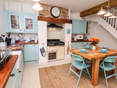A kitchen with blue cabinets wooden countertops a stove a wooden dining table with blue chairs and orange flowers at Navigators Rest in Whitby