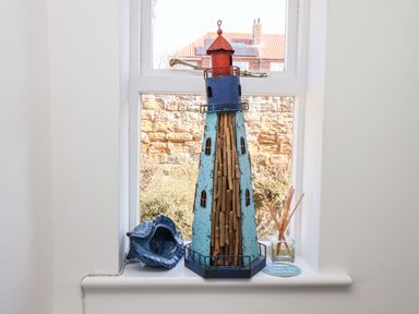 A window sill with a decorative lighthouse figure a blue ceramic shell and a reed diffuser at Navigators Rest in Whitby