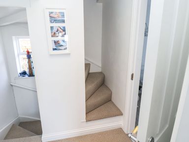 A hallway with carpeted stairs and a wall with framed pictures and a window with a lighthouse decoration at Navigators Rest in Whitby